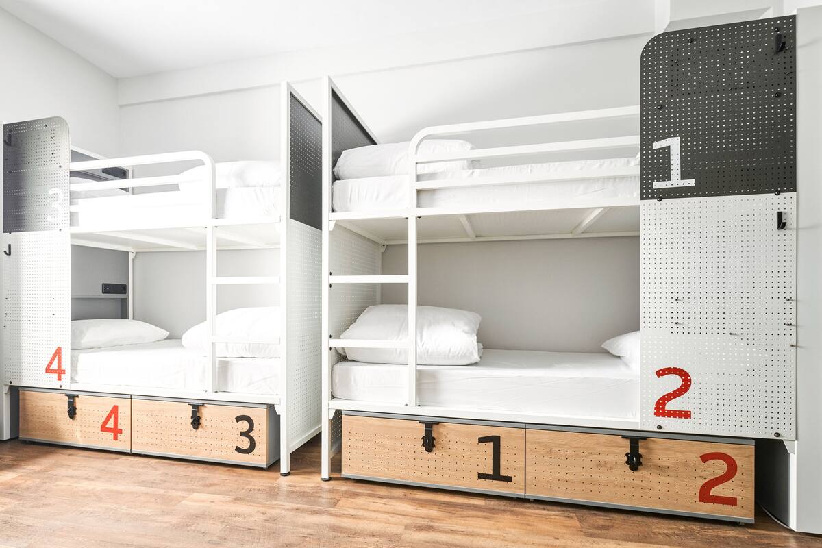 Habitación tipo dormitorio con literas, cajones de almacenamiento numerados y un panel perforado en la pared.
