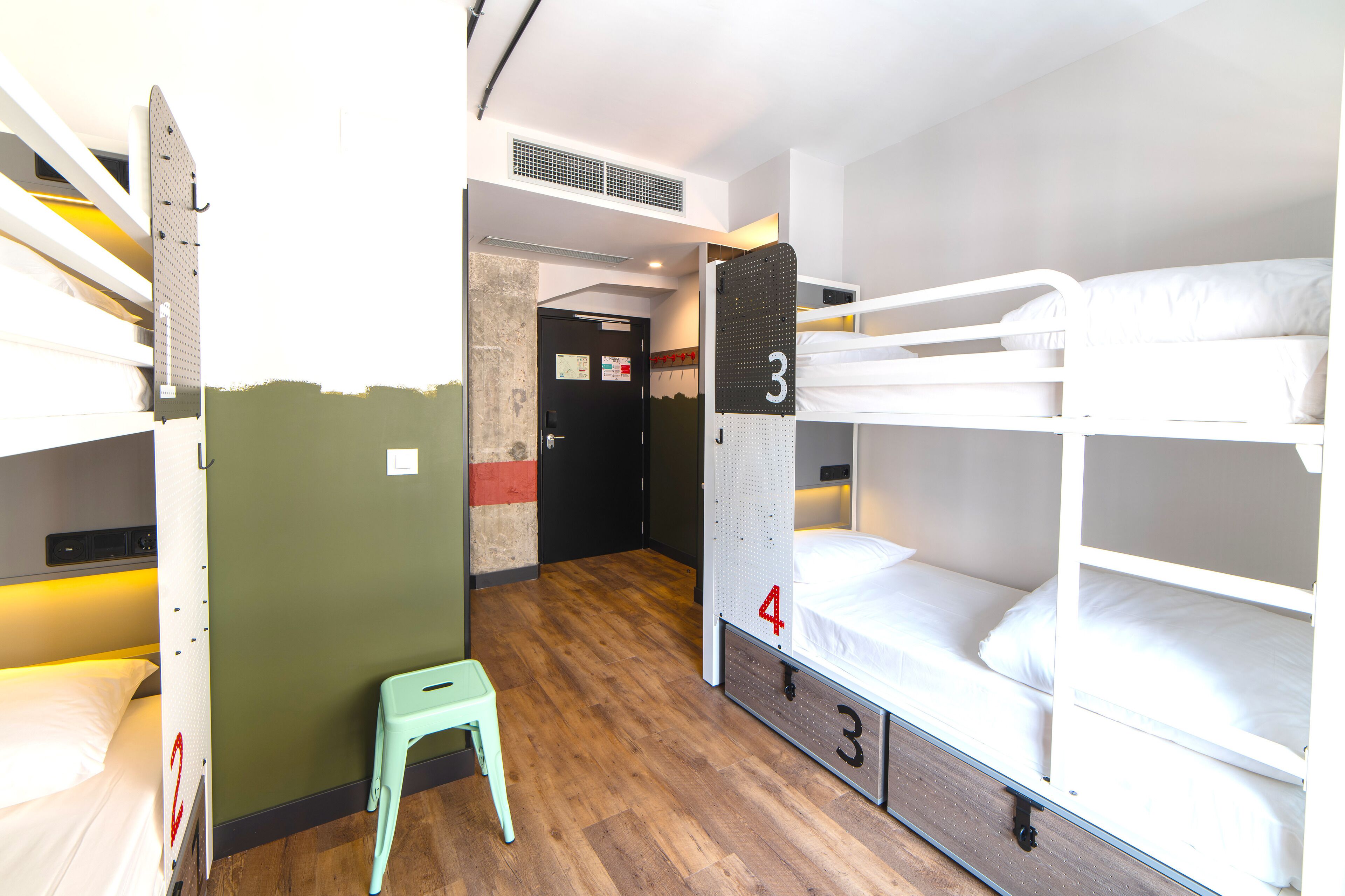 Une chambre de dortoir avec des lits superposés, un petit tabouret et une porte donnant sur une autre pièce.
