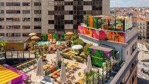 Un bar en la azotea con mesas al aire libre, piscina y vistas de la ciudad.