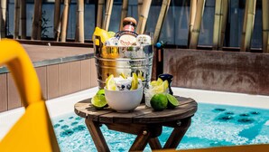 Escena junto a la piscina con una mesa de madera que sostiene una botella de tequila Don Julio, un cuenco con rodajas de lima y un tarro de vidrio con más rodajas de lima.