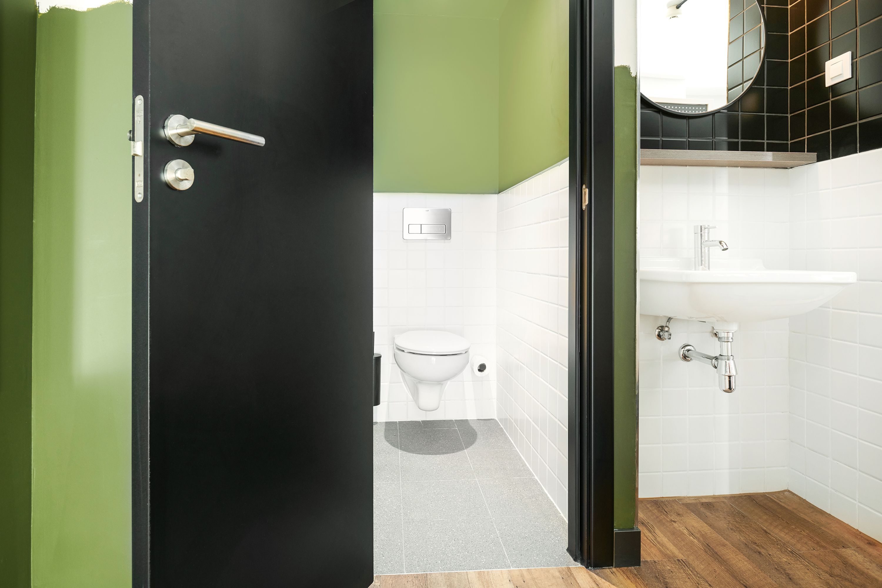 A modern bathroom with a black door, green walls, a white sink, and a toilet.