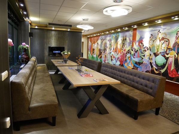Un restaurante con largas mesas de madera y bancos acolchados, un mural grande en la pared y un televisor de pantalla plana también en la pared.