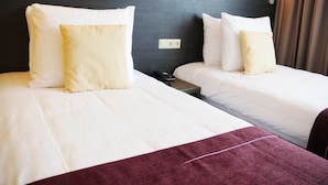 Une chambre d’hôtel avec deux lits, chacun doté de draps blancs et d’un oreiller à motifs. On y trouve une table de chevet avec un téléphone et une télécommande.