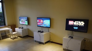 Une salle de jeux équipée de trois consoles affichant différents jeux, d’une table blanche et d’une fenêtre.