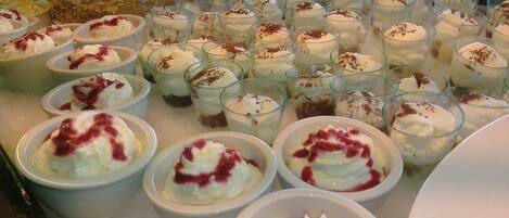 Uma mesa com sobremesas cremosas em taças e copos, algumas delas decoradas com chantilly e frutos vermelhos.