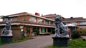 Un bâtiment avec deux statues de lions en pierre à l’entrée, un chemin pavé et un mur en briques.