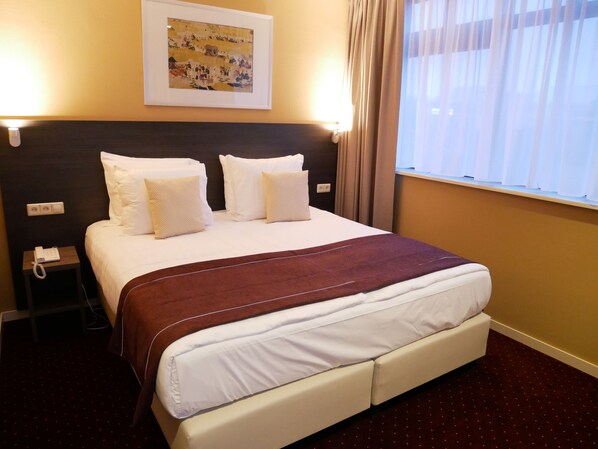 A hotel room with a large bed, white bedding, a brown headboard, a framed picture on the wall, a bedside telephone, and a window with curtains. - Hotel Het Oosten (Hazerswoude-Dorp)