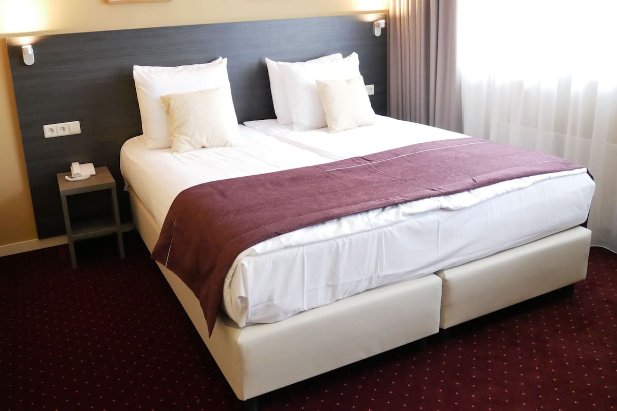 Una habitación de hotel con una cama grande, dos mesitas de noche, un teléfono sobre la izquierda y dos cuadros en la pared.