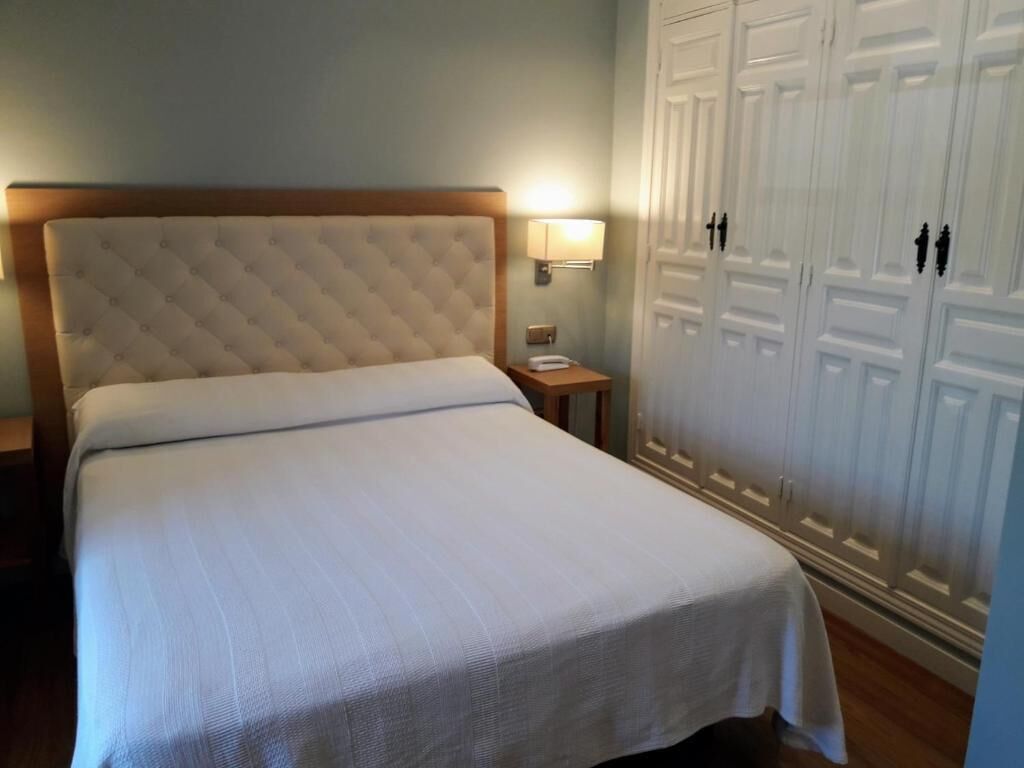 A neatly made bed with a wooden headboard, a bedside lamp, and a wardrobe with double doors.