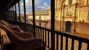 Wicker chairs on a balcony with a view of a historic building with a cross and statues.