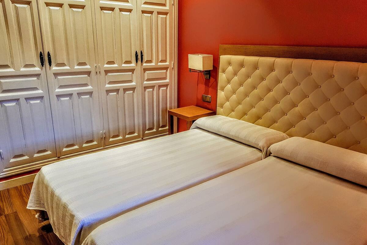 A double bed with a tufted headboard, a bedside table with a lamp, and a wardrobe with a mirrored door.