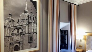 A hotel room with a framed black and white photo of a historic building, a bed, a bedside table, and a nightstand.