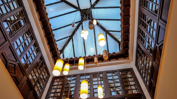 A high-ceilinged room with a skylight, wooden lattice windows, and hanging cylindrical lamps.