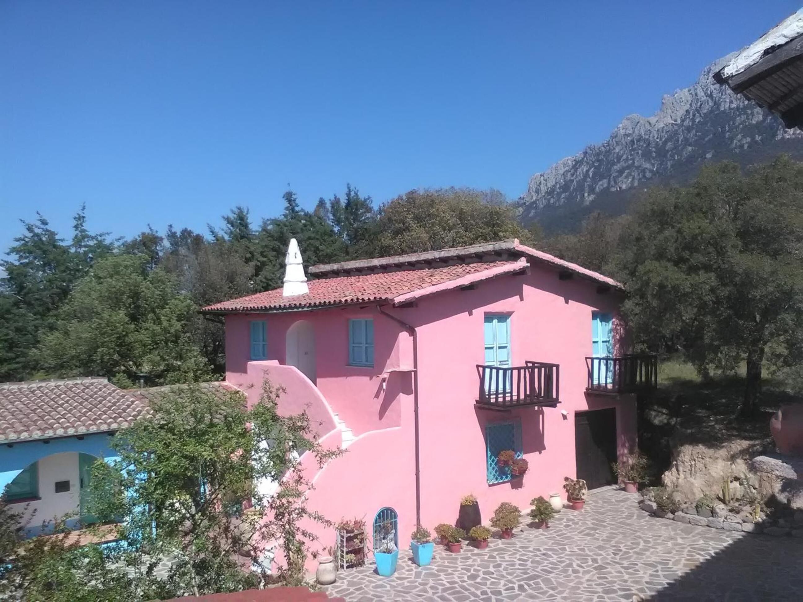 A pink building with a tiled roof, a balcony, and potted plants in the foreground.