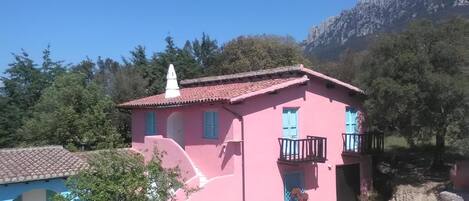 A pink building with a tiled roof, a balcony, and potted plants in the foreground.