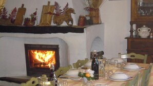 Comedor con chimenea, sillas verdes, mesa servida con platos, vasos y una jarrón de agua.