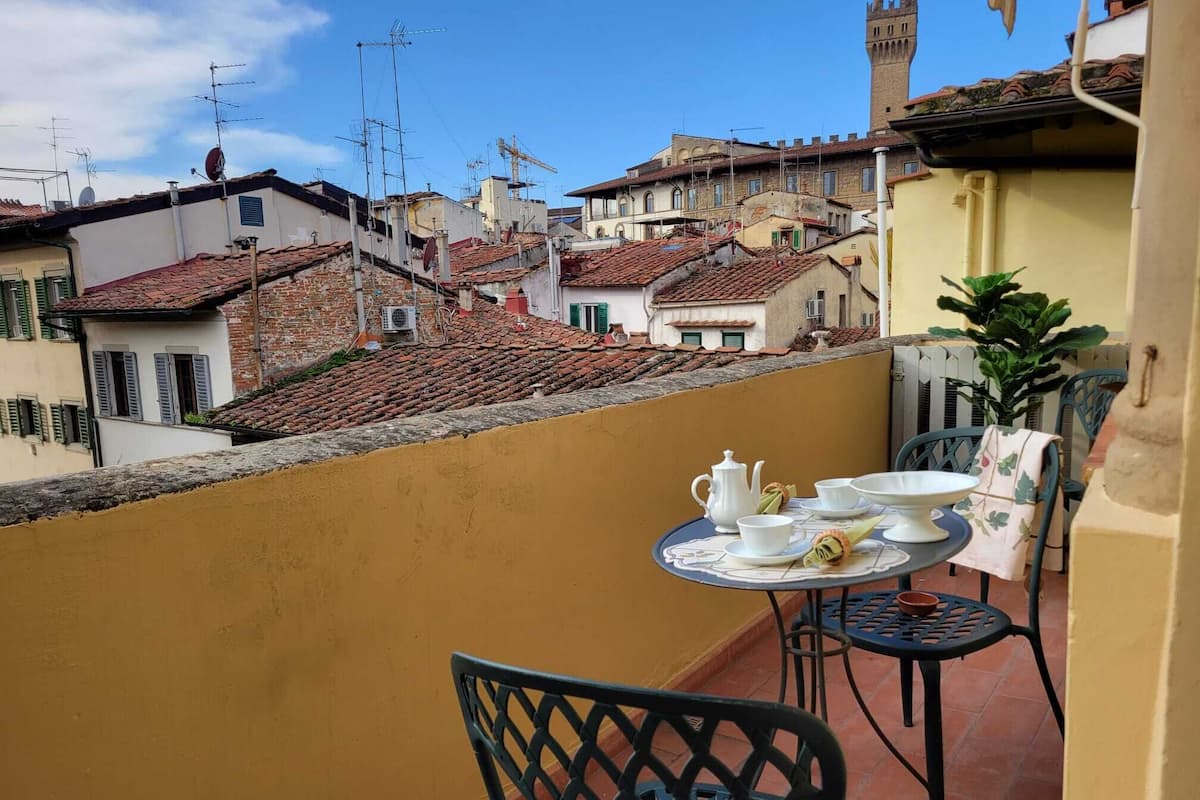 A balcony with a table set for tea, overlooking a cityscape with historic buildings and a tower.