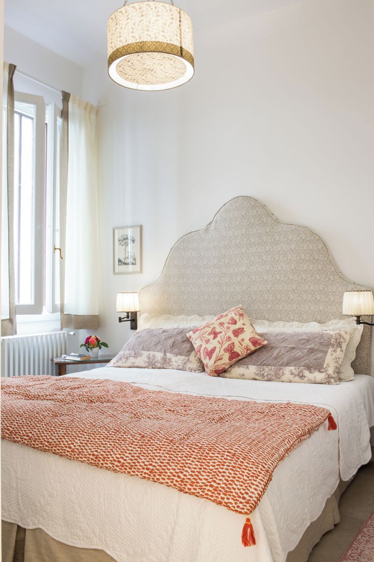 A hotel room with a large bed, two bedside tables, a window with curtains, a radiator, and a hanging light fixture.
