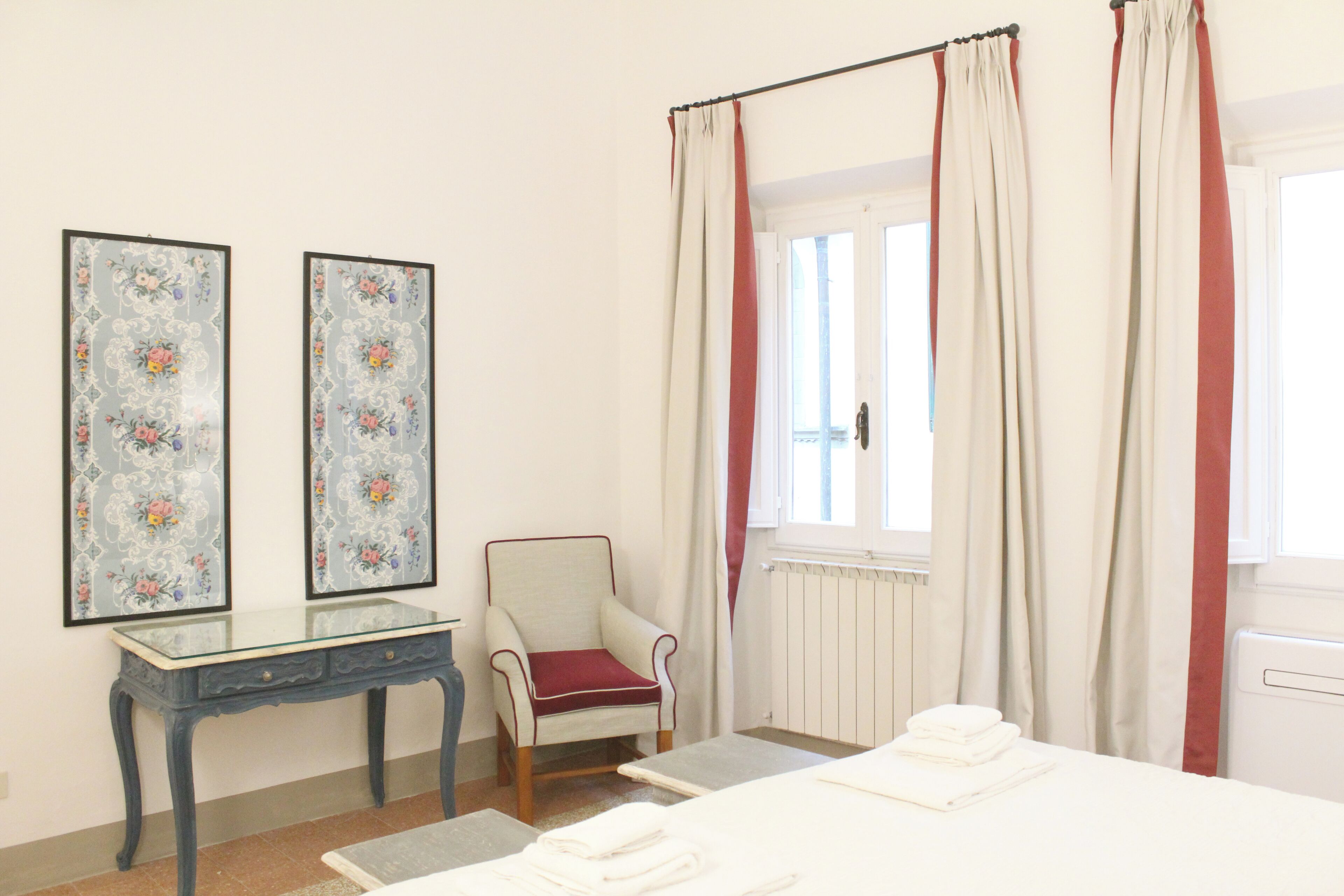 A bedroom with a bed, a chair, a table, and two framed floral artworks.