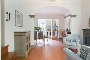 A spacious living room with a fireplace, a dining area with chairs, and a kitchen visible through an archway. - Borgodegreci Apartments (Florence)