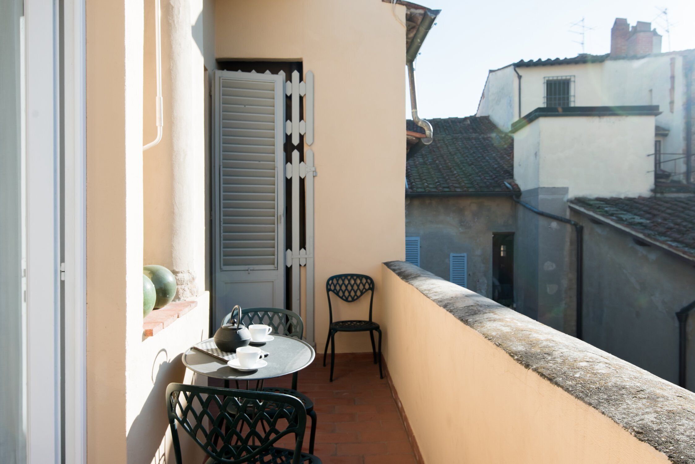 Ein Balkon mit Tisch und Stühlen, eine Tür mit Rollläden und Blick auf benachbarte Gebäude.