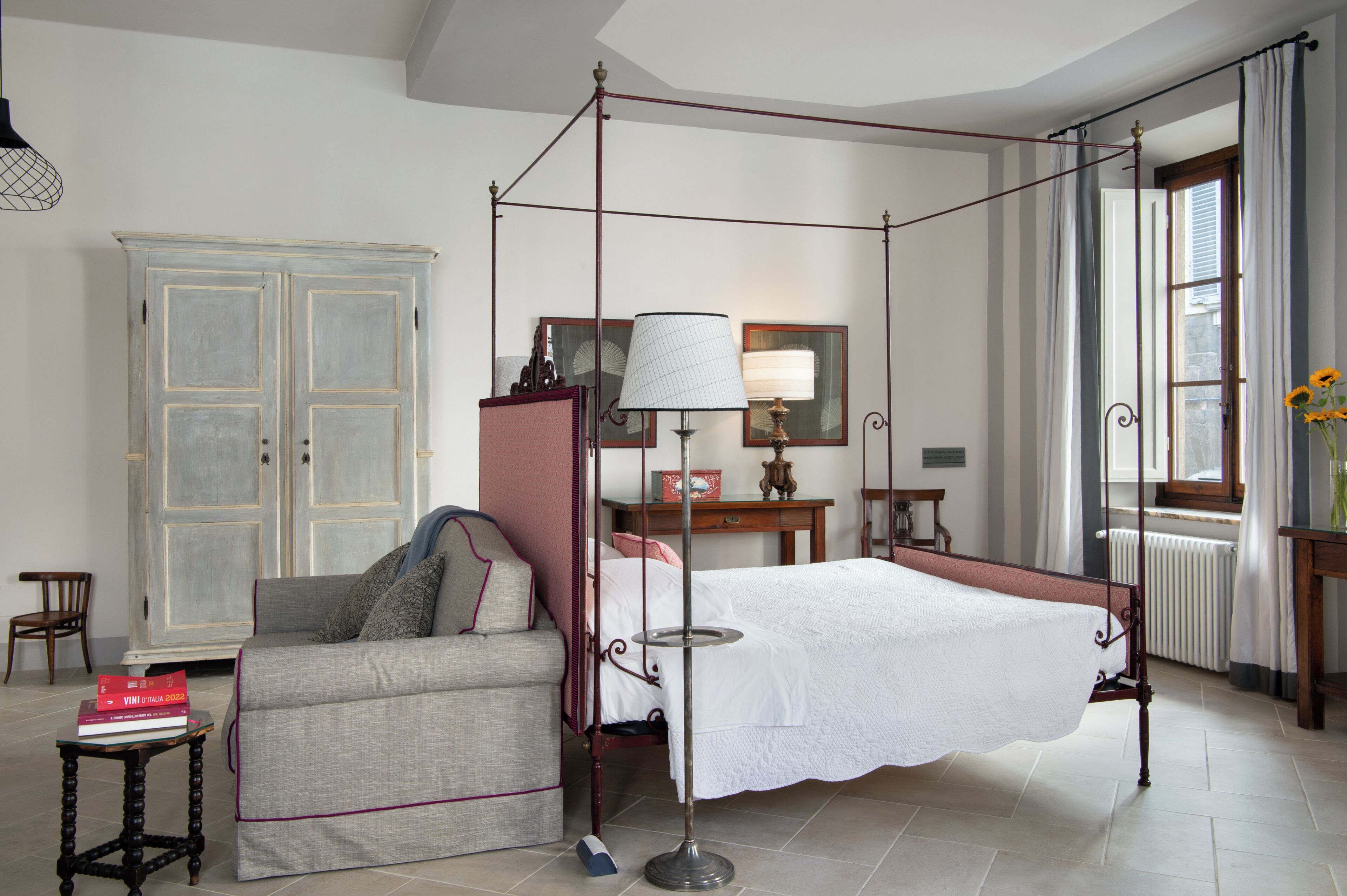 Une chambre à coucher avec un lit à baldaquin, un canapé, une armoire, une table avec des livres et une fenêtre avec des rideaux.