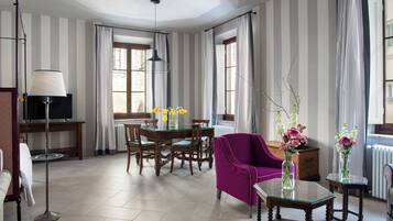 Une chambre d’hôtel avec un coin repas, un fauteuil violet, une table en verre et un téléviseur.