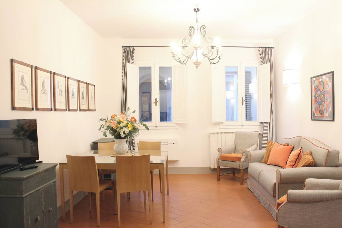 A living room with a dining table, chairs, a sofa, a TV, and framed artwork on the wall.