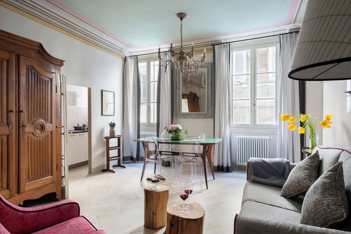 A spacious living room with a wooden cabinet, a glass dining table, and a sofa with patterned cushions.