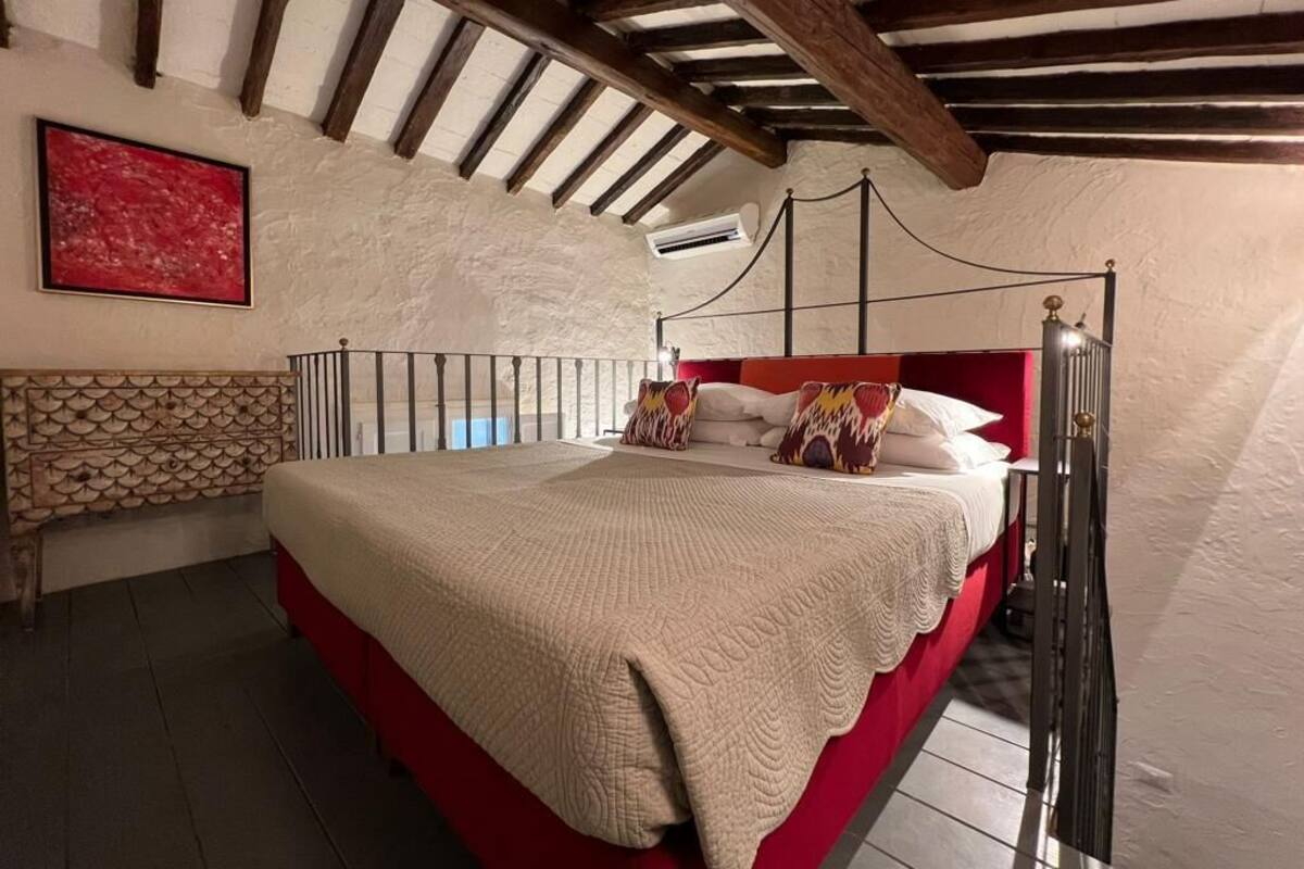 A bedroom with a red bed, a white wall, and a wooden ceiling.