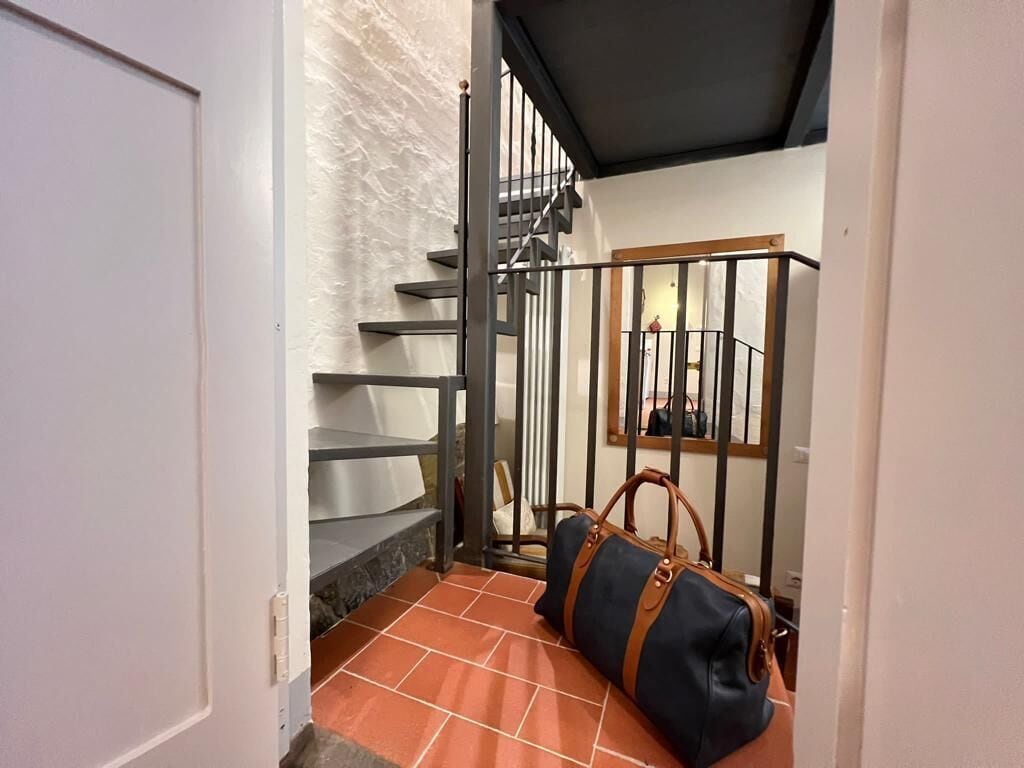 Una escalera con barandilla de metal, un bolso en el suelo y un espejo en la pared.