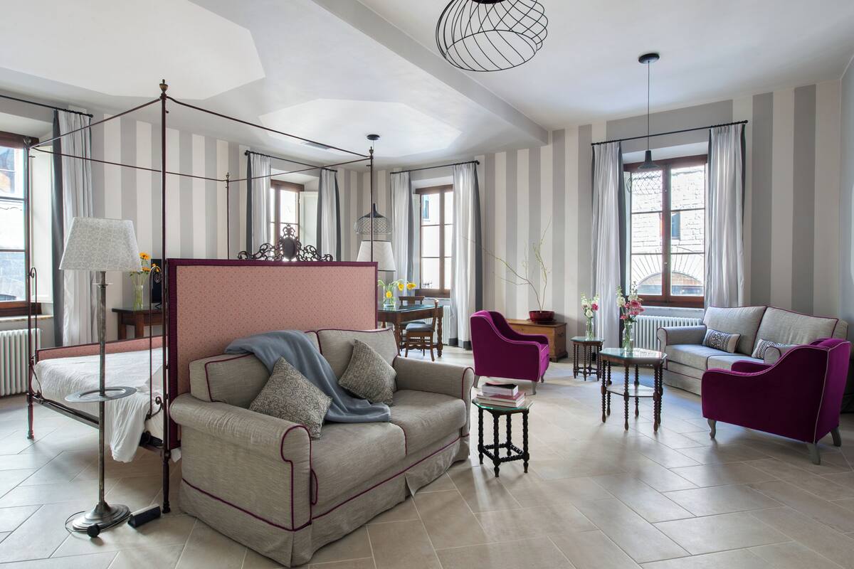 A spacious room with a four-poster bed, a sofa, a loveseat, and a dining area with a table and chairs.
