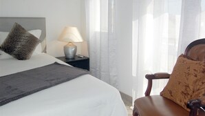 A neatly made bed with a grey throw, a lamp on a bedside table, and a chair with a patterned cushion. - Suites Inn Lagos (Lagos)