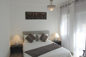 A neatly arranged bedroom with a bed, two bedside tables with lamps, a chandelier, and a wall-mounted artwork. - Suites Inn Lagos (Lagos)