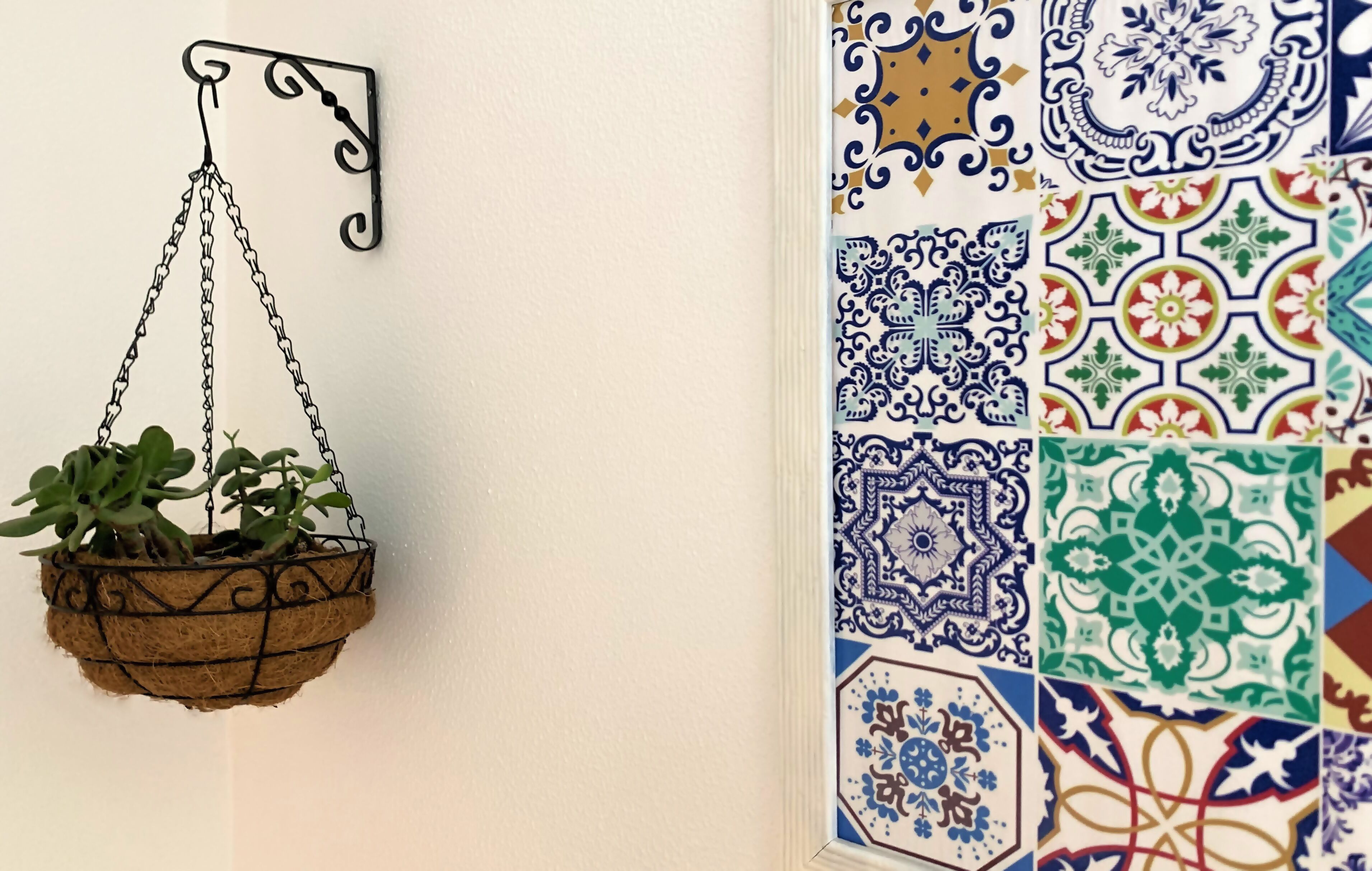 Una planta colgante con estructura metálica rústica frente a una pared con un diseño de azulejos decorativos.