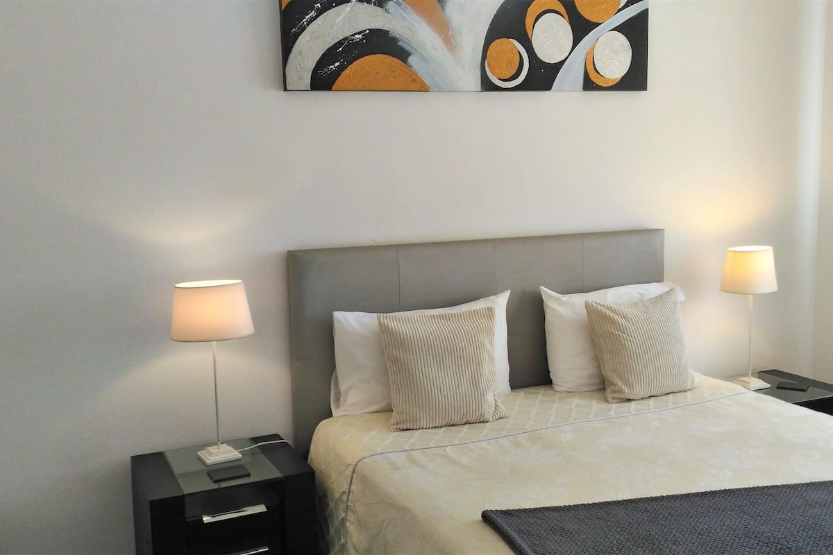 A hotel room with a bed, two bedside tables, a nightstand, a lamp, and a painting on the wall.