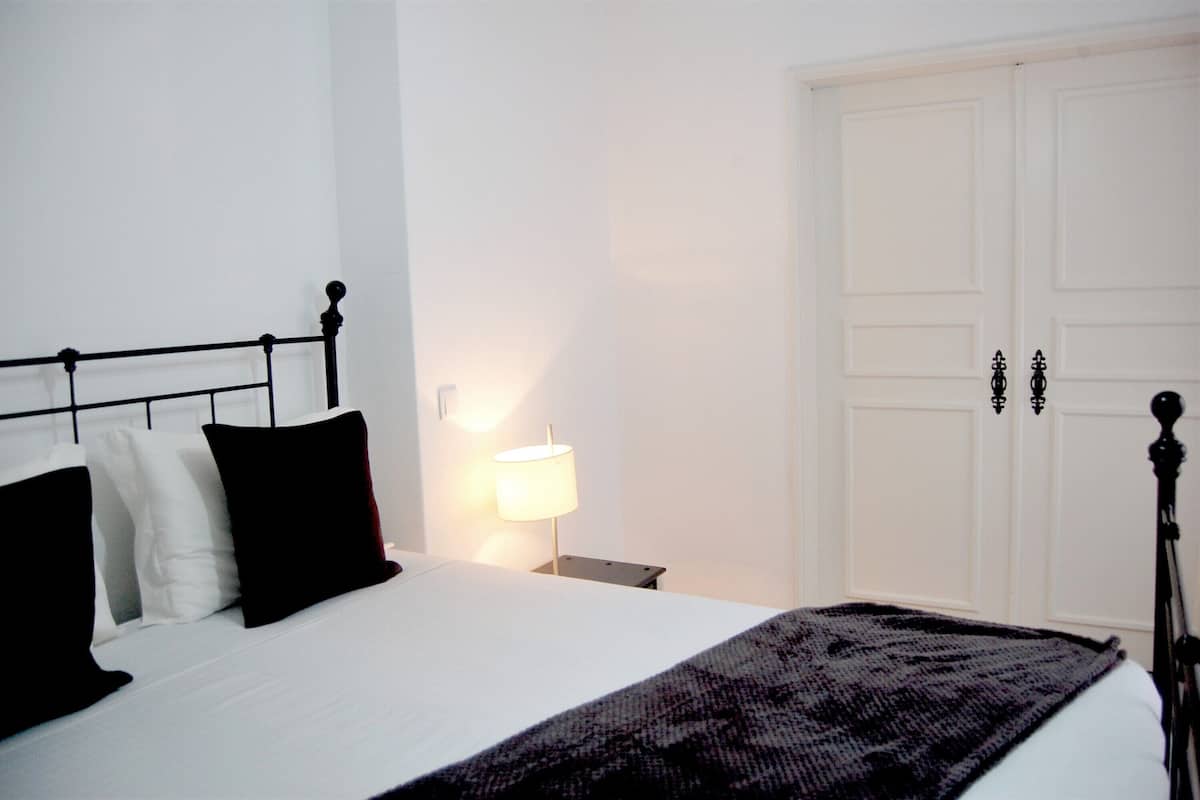 A bedroom with a bed, a nightstand, a lamp, and a wardrobe.