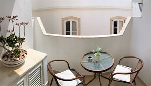 A balcony with a potted plant, two wicker chairs, a small table with a glass top, and a view of a building with windows. - Suites Inn Lagos (Lagos)