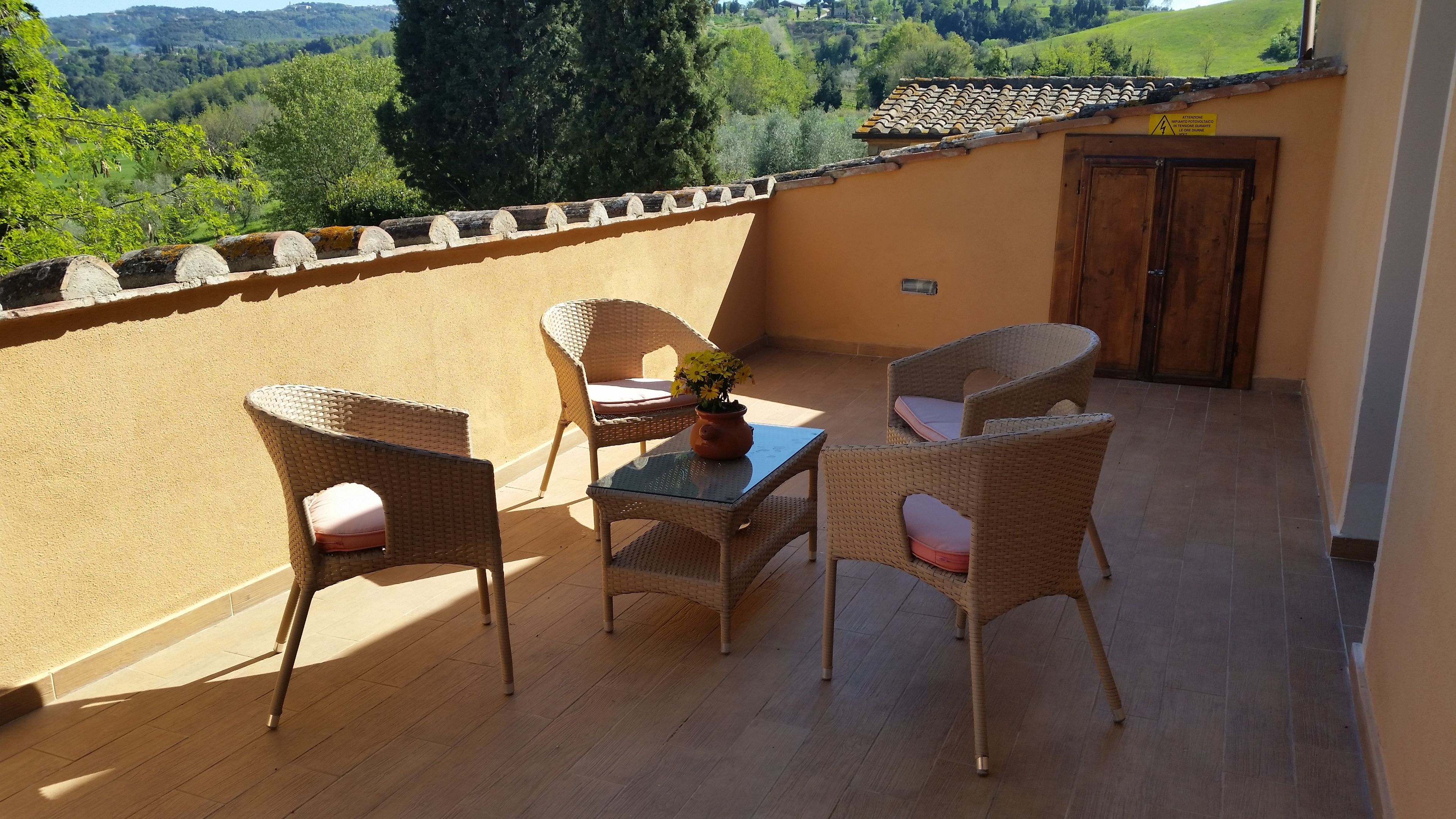 A balcony with wicker chairs, a table, and a potted plant.