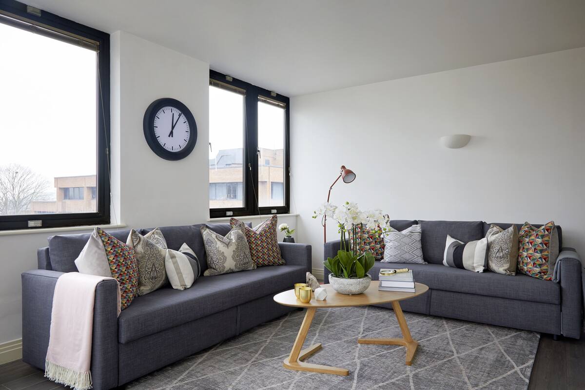 A modern living room with a grey sofa, patterned cushions, a round coffee table, and a large window with a view of buildings.