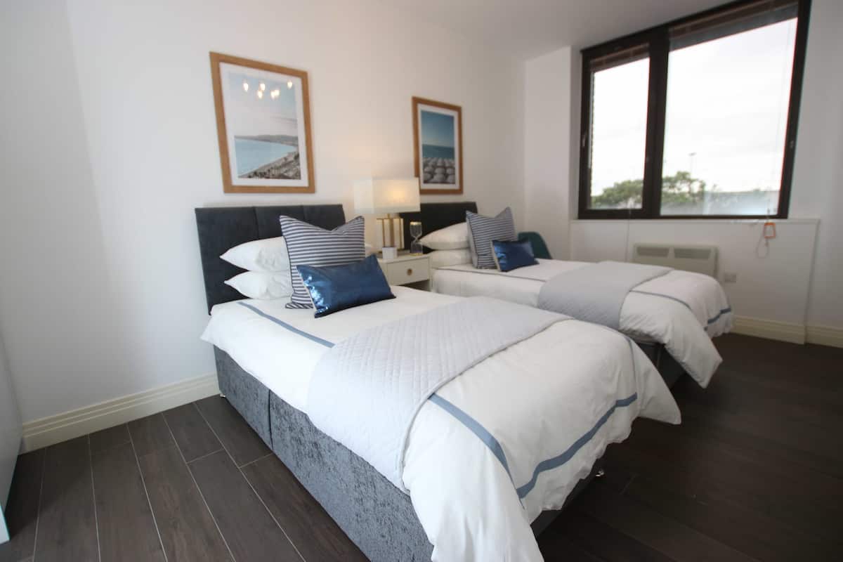 A hotel room with two beds, a large window, and framed pictures on the wall.