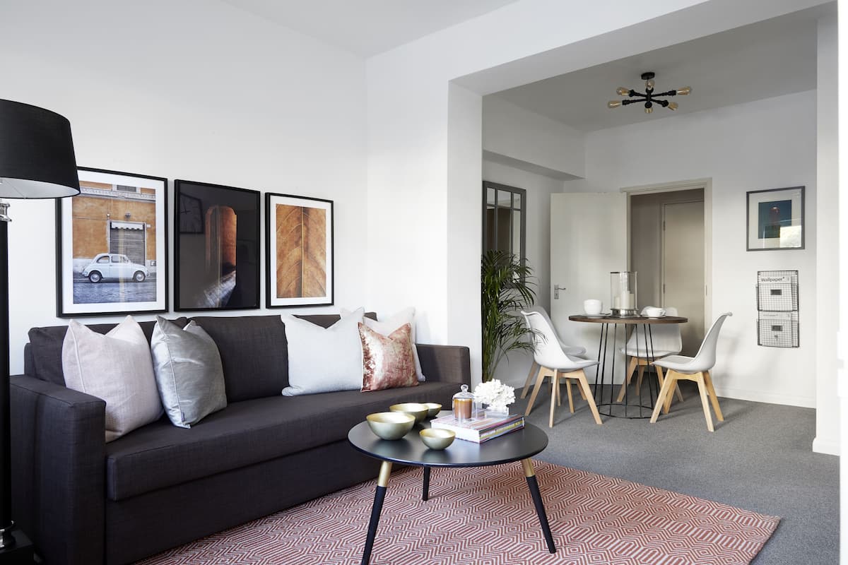 A modern living room with a dark grey sofa, a coffee table, and a dining area with a small table and chairs.