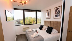 Une chambre d’hôtel moderne dotée d’un grand lit, de deux tables de chevet, d’une fenêtre donnant sur la ville et d’œuvres d’art encadrées accrochées au mur.