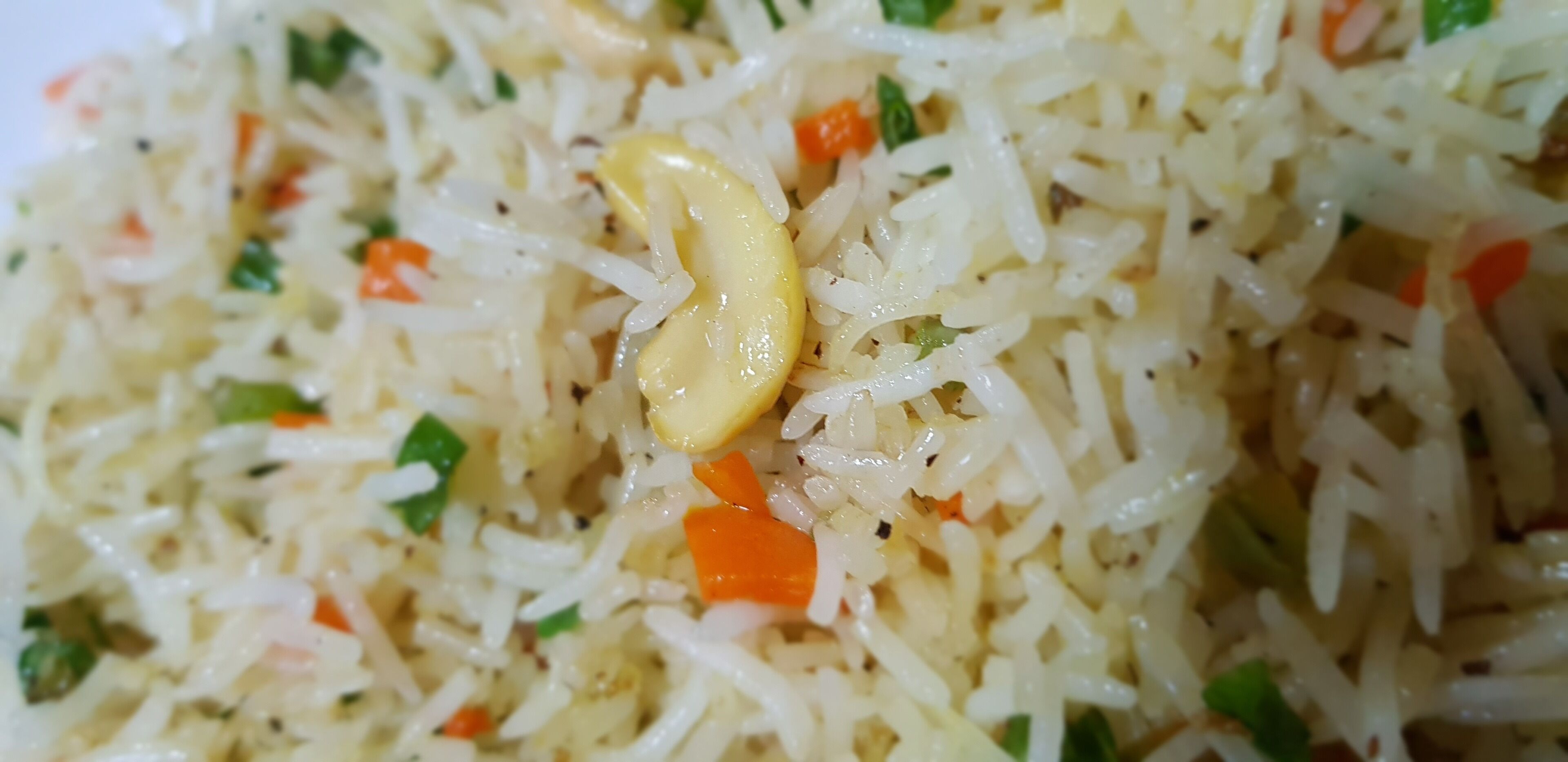 A close-up of a dish with rice, carrots, and green herbs.