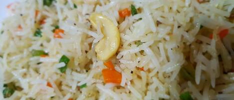 A close-up of a dish with rice, carrots, and green herbs.