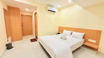 A hotel room with a bed, bedside table, and an air conditioning unit.