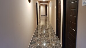 Un pasillo con suelo de mármol, paredes color beige y puertas de madera oscura.