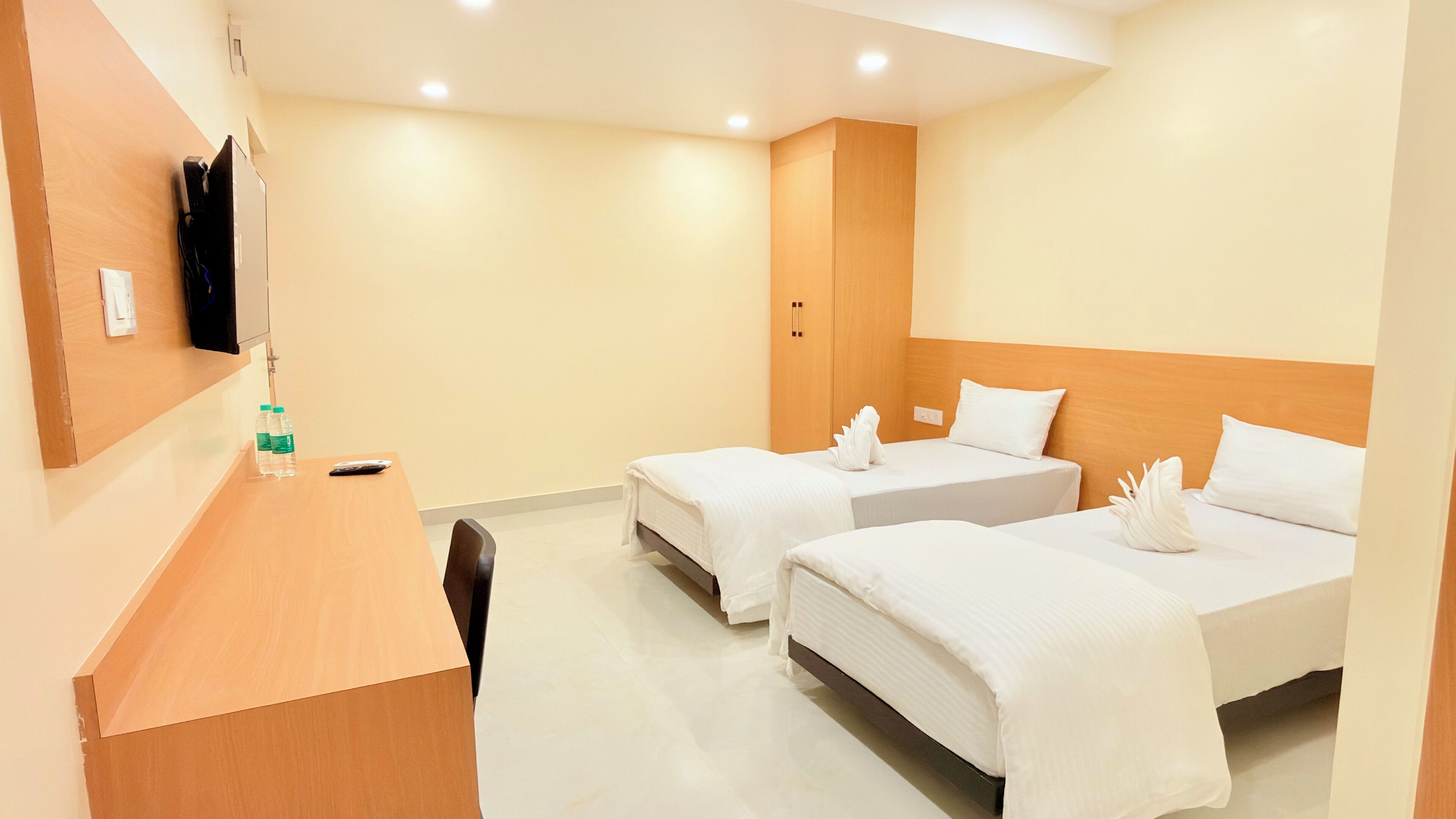 A hotel room with two beds, a wooden desk, and a television on the wall.