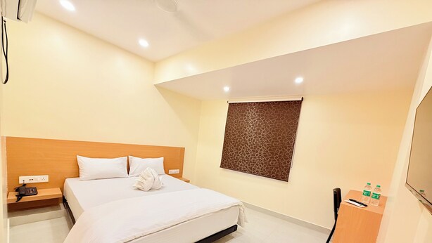 Habitación de hotel con una cama, una mesita de noche con un teléfono, una obra de arte colgada en la pared y una pequeña mesa de madera con dos botellas.