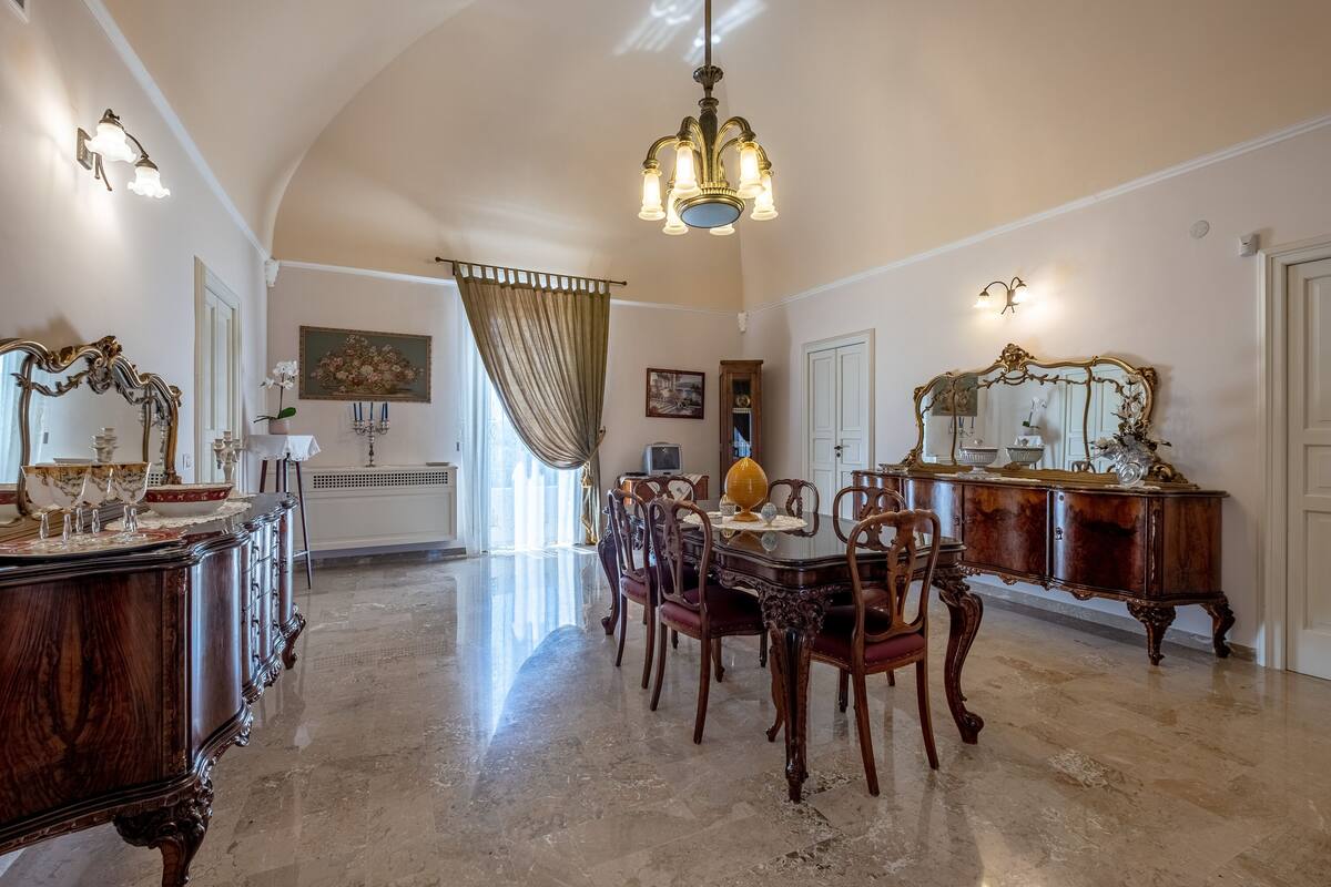 Un comedor amplio con techo alto, candelabros elegantes y mobiliario clásico.